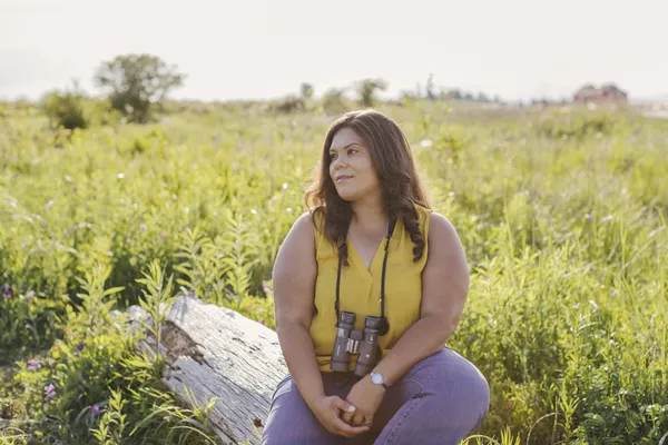 Someone sitting on a log with binoculars around their neck