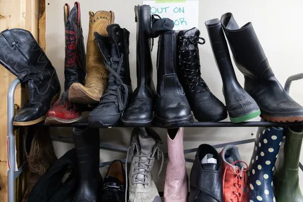 Several individual boots, including black, brown and pink leather cowboy boots, rubber boots and lace-up winter boots in the back room of a Winnipeg thrift store