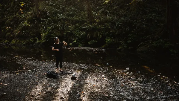 An artist playing sounds in the forest near running water.