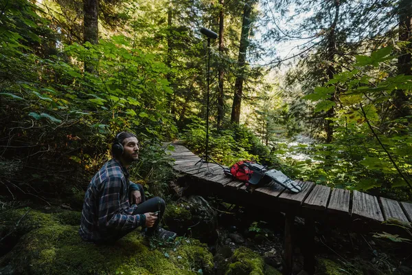 An artist recording and listening to sounds in the forest